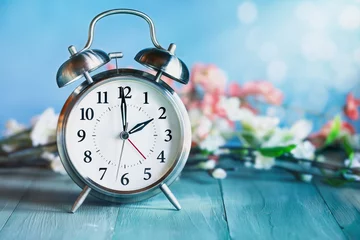 Foto op Canvas Set your clocks forward with this clock and flowers over a rustic teal wooden table. Daylight saving time concept. Selective focus with blurred background. © Stephanie Frey