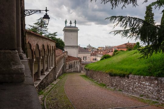 Pedestrian path along renaissance Venetian gothic style arcade leading to castle of Udine, Friuli Venezia Giulia, Italy, Europe. Column, arch architecture. View on clock tower on Piazza della Liberta