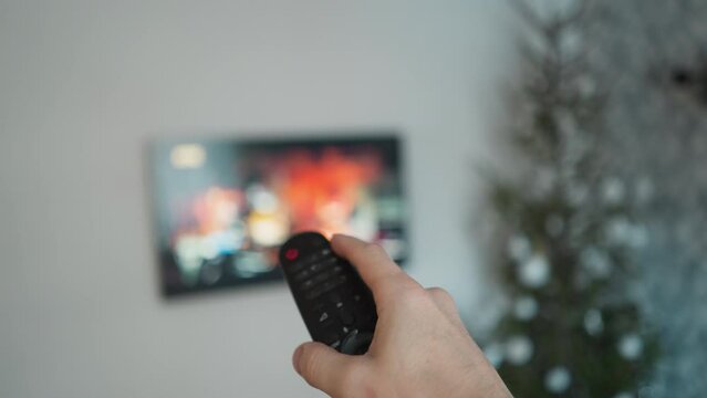Person channel surfing with a TV remote, Christmas tree in the background, POV with a handheld camera