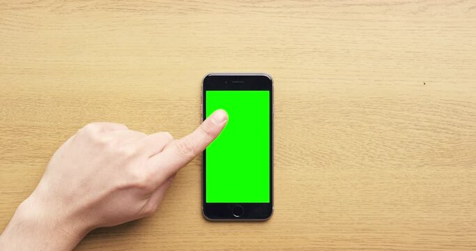Hands, phone and green screen on desk in closeup with typing, scroll and click on ui for promotion. Smartphone, finger and user experience with mock up space for mobile app, website or social media