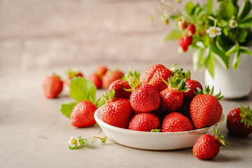 Heap of fresh ripe strawberries in ceramic bowl on rustic light background.