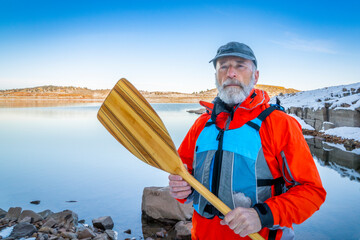 senior canoe paddler wearing life jacket on a shore of Carter Lake in northern Colorado in winter...