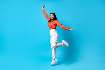 Fototapeta na wymiar Joyful carefree Indian young woman jumps and raises arm, studio
