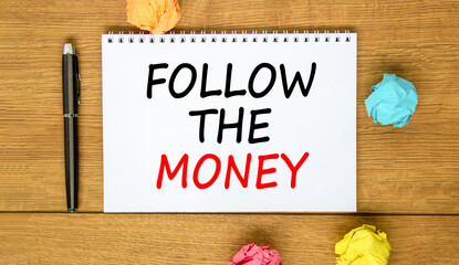 Naklejka premium Follow the money symbol. Concept words Follow the money on beautiful white note. Beautiful wooden background. Black pen. Colored paper. Business and follow the money concept. Copy space.