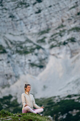 Fototapeta premium Young woman meditating on a rock in high mountains