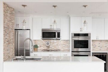 A kitchen detail with white cabinets, a brown stone and glass tile backsplash, and bronze lights...