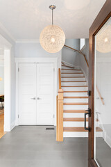 Foyer entryway of a home with a wood and glass front door, a hanging light, and looking towards the...