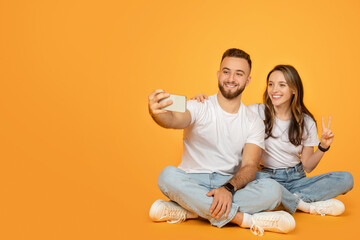 A young, seated couple happily engaged in taking a selfie, with the man holding the phone