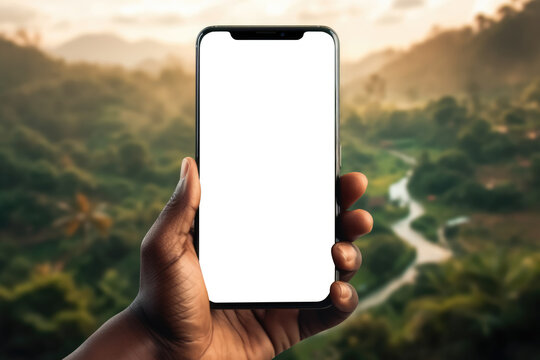 Afro American man's hand delicately holds a phone with a blank screen, poised as a mockup against the tranquil backdrop of a verdant landscape