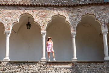 Female model standing between columns and arches of renaissance Venetian gothic style arcade...