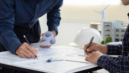 Engineers are helping to design work on blueprints with wind turbine model. Eco-friendly building....