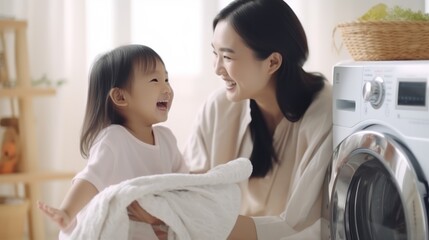 Asian woman sitting in front of a washing machine to her cute daughter to smell after cleaning it in a laundry room at home. - obrazy, fototapety, plakaty