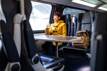 Smiling women listening to music and drinking coffee while traveling high speed train. - obrazy, fototapety, plakaty