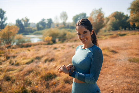 A portrait of a happy young athletic woman adjusting her smart watch and preparing for a jog in nature