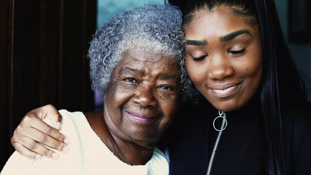 Happy portrait of young African American granddaughter with arm around her grandmother posing for camera, close-up faces of intergenerational family members embrace