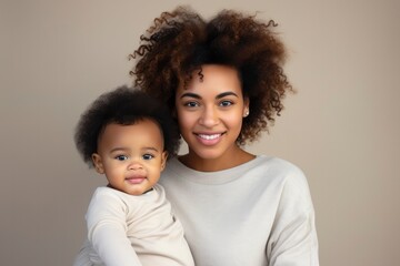 Happy motherhood, family, love. Young beautiful smiling African American woman with a baby in her arms on beige background, portrait. Black girl with child, mother's day