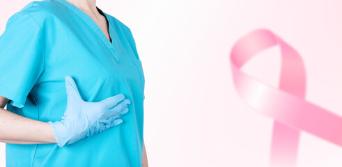 A female doctor in a medical uniform supports her breasts and a pink ribbon as a symbol of breast cancer awareness. Medical pink background. Poster. copy space.