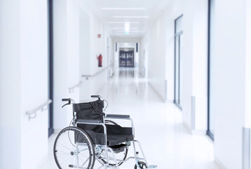 Empty wheelchair in modern hospital corridor interior in light colors. Soft blurred background.