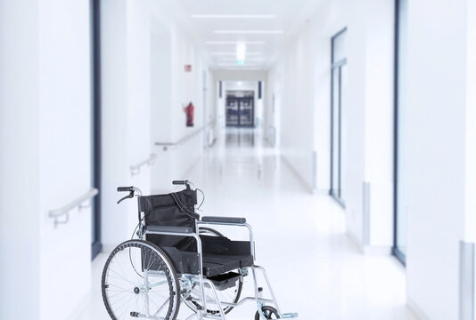 Empty wheelchair in modern hospital corridor interior in light colors. Soft blurred background.