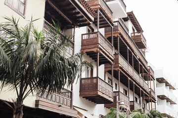 Fototapeta premium Exotic island architecture. Block of flats in Spain. Living in paradise. Real estate market in Spain background. Palm tree near balcony. Sunny day building. Holiday flat rental. Wooden balcony.