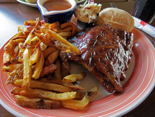 Barbecued pork spareribs with a bun, coleslaw, and French fries.