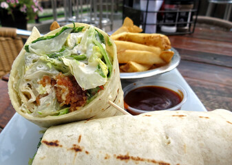 Closeup of the inside of a chicken Caesar wrap, served with French fries, out on the patio