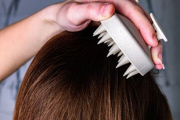 Fototapeta premium Young woman doing self hair scalp massage with scalp massager for hair growth stimulating at home.