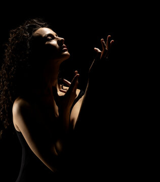Sensual portrait silhouette of beautiful curly woman with outstretched hand sings in backlight on a black background