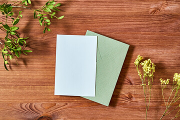 Mockup invitation or blank greeting card and envelope with green leaves on a wooden background