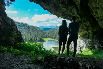 Hiking couple standing in dark cave Drachenhoehle with panoramic view of alpine lake Sackwiesensee...