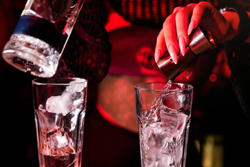 Bartender pours alcohol into a glass with ice using a jigger. Mixing an alcoholic cocktail in a nightclub, pub, restaurant