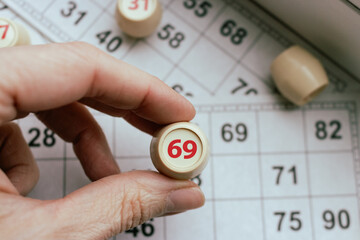 Playing lotto game. Person holding cube with figure on bingo card background. Nostalgia lifestyle. Table games. Retro games. Barrel with number 69 and paper cards for bingo game. Holiday leisure. 