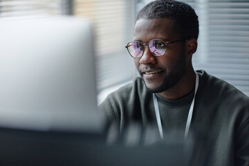 Closeup portrait of professional Black young man wearing glasses with computer screen reflection in...