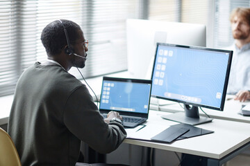 Side view portrait of Black young man wearing headset as client support operator at data security...