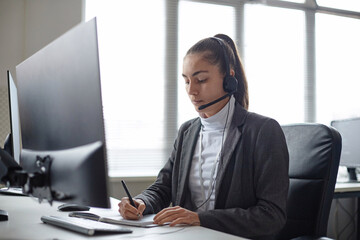 Side view portrait of young woman speaking into headset with microphone while consulting client on...