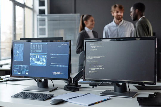 PC computers with code lines and blue data on screen at desk in cybersecurity company with diverse team in blurred background copy space