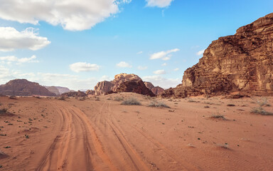 Red orange sandstone rocks formations in Wadi Rum desert, vehicle tire prints in sand road near