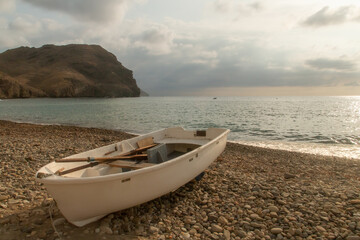 Una barca de remos tradicional varada en la playa. Playa de Las Negras al amanecer con el conocido como colina Negra al fondo. Almería, Andalucía, España.