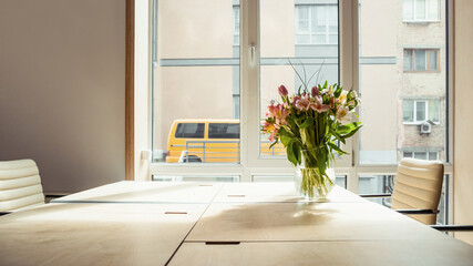 Empty room with table near the window and few chairs near that. Sunlight coming from behind. Flowers in a vase on the table. 