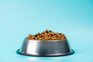 Brown cat or dog kibble in a metal bowl isolated top view close-up. Nutritious healthy diet pet food scattered around, falls and cascades the bowl. Dry cat or dog food spills from a bowl.