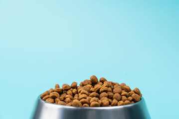 Brown cat or dog kibble in a metal bowl isolated top view close-up. Nutritious healthy diet pet food scattered around, falls and cascades the bowl. Dry cat or dog food spills from a bowl.
