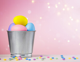multicolored eggs are collected in a metal bucket on a pink background