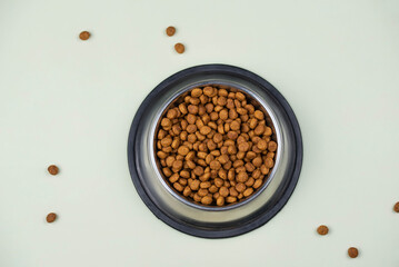Brown cat or dog kibble in a metal bowl isolated top view close-up. Nutritious healthy diet pet food scattered around, falls and cascades the bowl. Dry cat or dog food spills from a bowl.