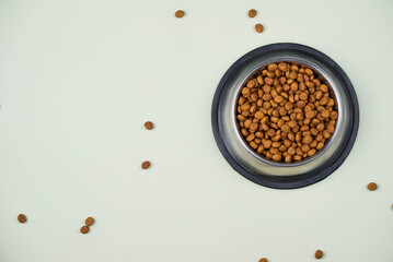 Brown cat or dog kibble in a metal bowl isolated top view close-up. Nutritious healthy diet pet food scattered around, falls and cascades the bowl. Dry cat or dog food spills from a bowl.