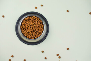Brown cat or dog kibble in a metal bowl isolated top view close-up. Nutritious healthy diet pet food scattered around, falls and cascades the bowl. Dry cat or dog food spills from a bowl.