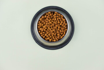 Brown cat or dog kibble in a metal bowl isolated top view close-up. Nutritious healthy diet pet food scattered around, falls and cascades the bowl. Dry cat or dog food spills from a bowl.