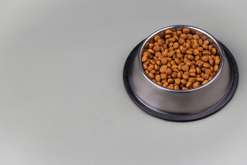 Brown cat or dog kibble in a metal bowl isolated top view close-up. Nutritious healthy diet pet food scattered around, falls and cascades the bowl. Dry cat or dog food spills from a bowl.