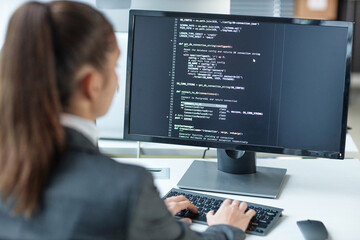 Over shoulder view of female programmer using computer with code lines on screen in IT company office copy space