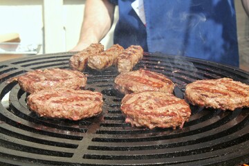 Grilled hamburger meat at barbecue in home backyard. Burgers cooking on gas grill with smoke outdoor. Process of preparing cutlet on grill with burning coals. Street food eat cafe on open fire