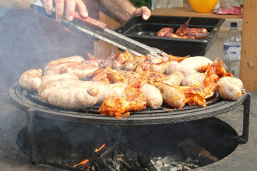 Fried sausages and chicken wings on barbecue grill in the village. Frying meat on open fire. Barbecue party on backyard of country house cabin. Street food festival. Home cooking outdoor. Picnic time